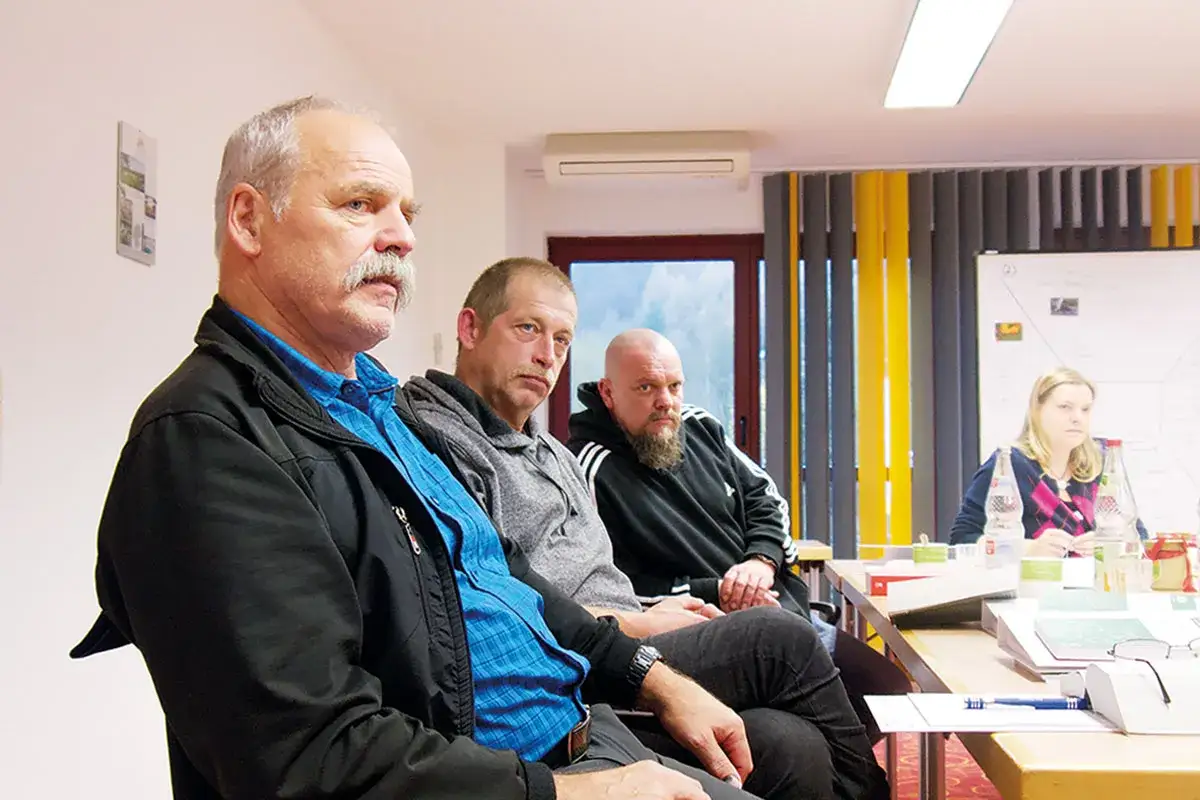 M&auml;nner und eine Frau sitzen an einem Tisch, diskutieren die Voraussetzungen f&uuml;r Kurzarbeit.