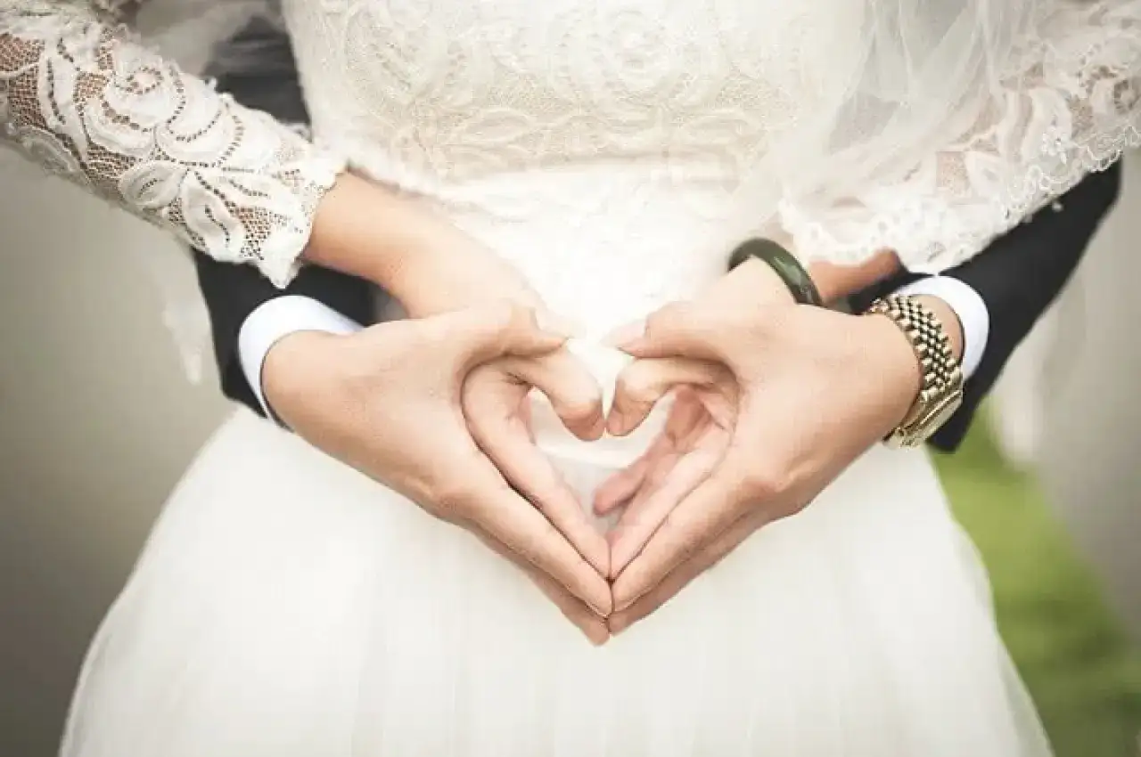 Brautpaar formt Herz mit H&auml;nden. Ein besonderer Moment der Liebe, der auf eine gl&uuml;ckliche Zukunft mit Kind hoffen l&auml;sst. Sonderurlaub Hochzeit Kind.