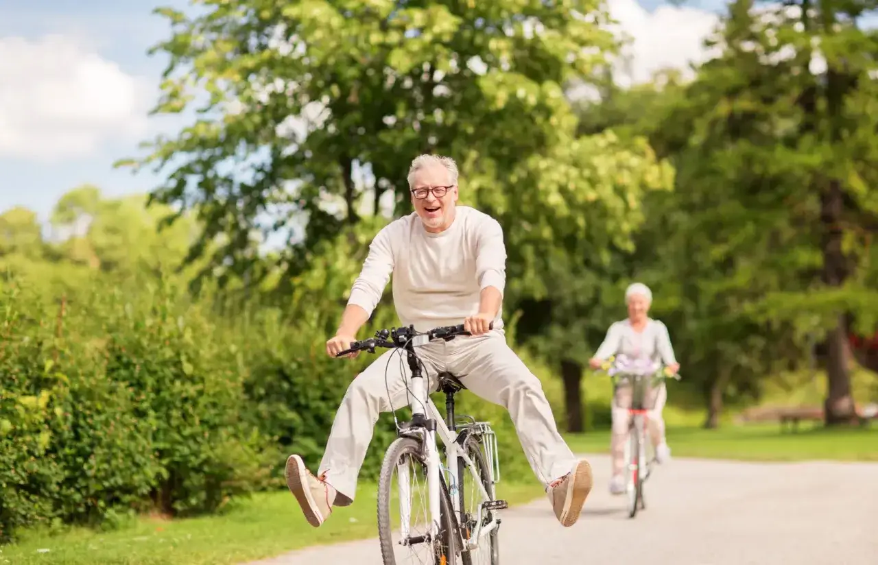 Ein Mann im engagierten Ruhestand lacht und fährt ausgelassen Fahrrad, während im Hintergrund eine Frau auf ihrem Rad fährt.