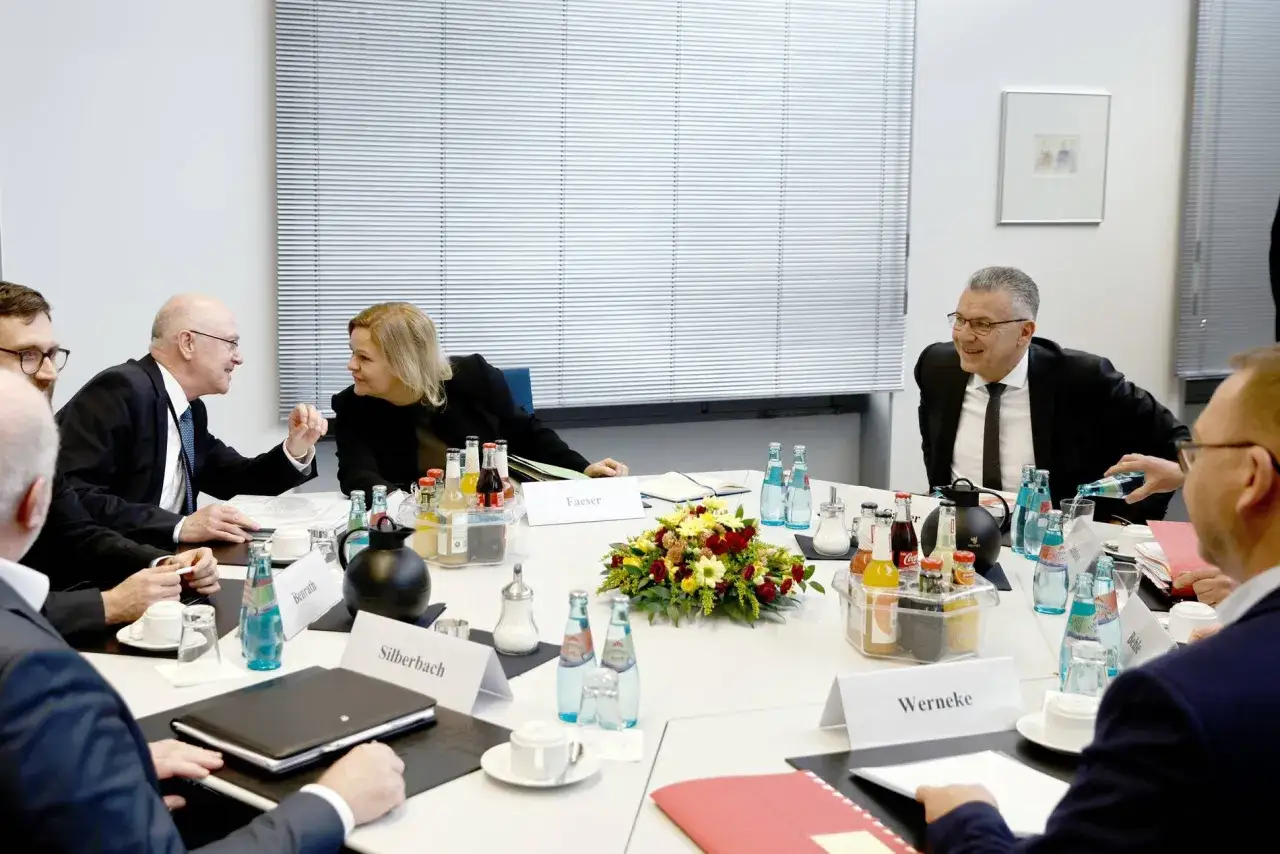 Diskussion am Tisch: Was heißt Verdi? Eine Frau und Männer im Anzug sprechen, Getränke und Blumen stehen bereit.