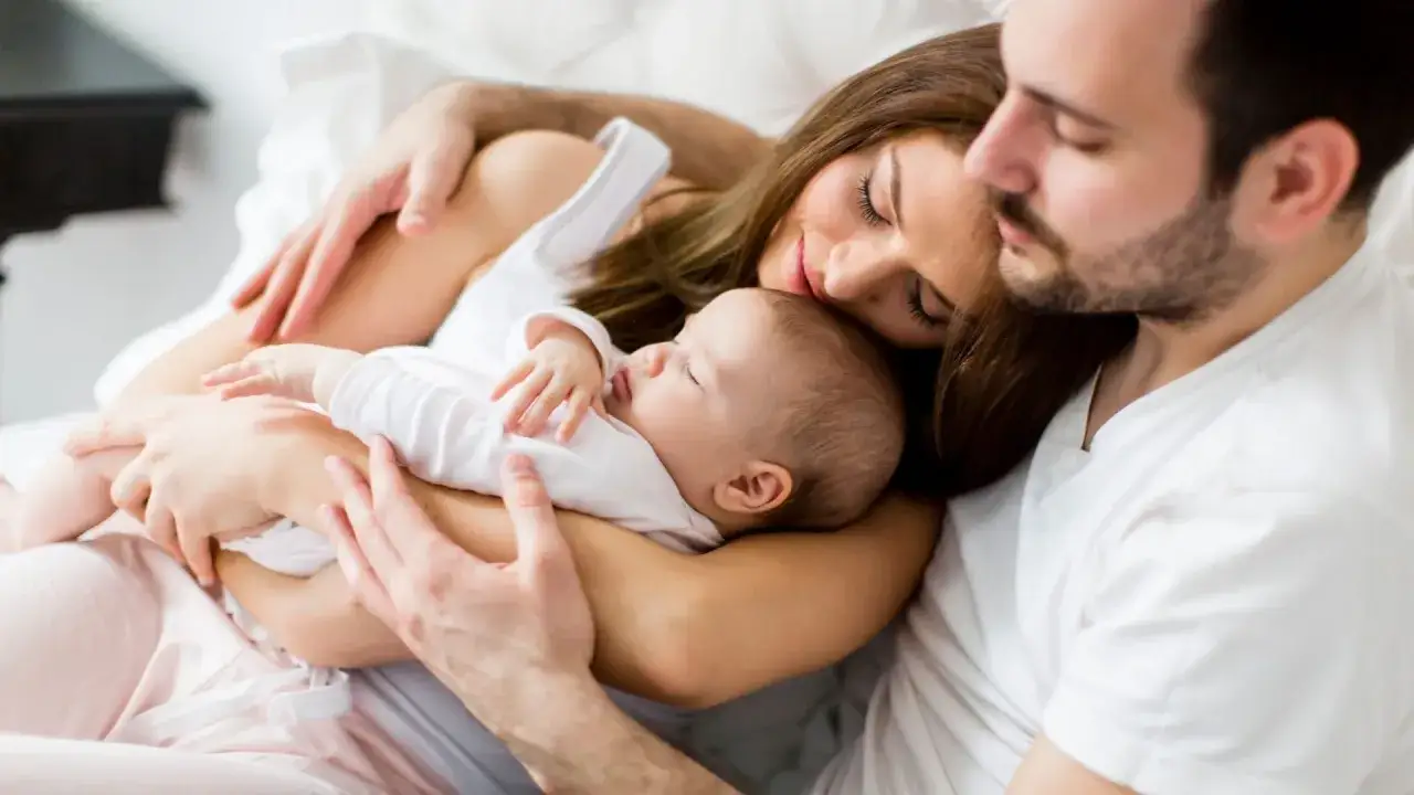 Glückliche Familie im Bett. Mutter und Vater halten ihr Baby, das friedlich schläft. Ein Moment des Sonderurlaubs nach der Geburt.