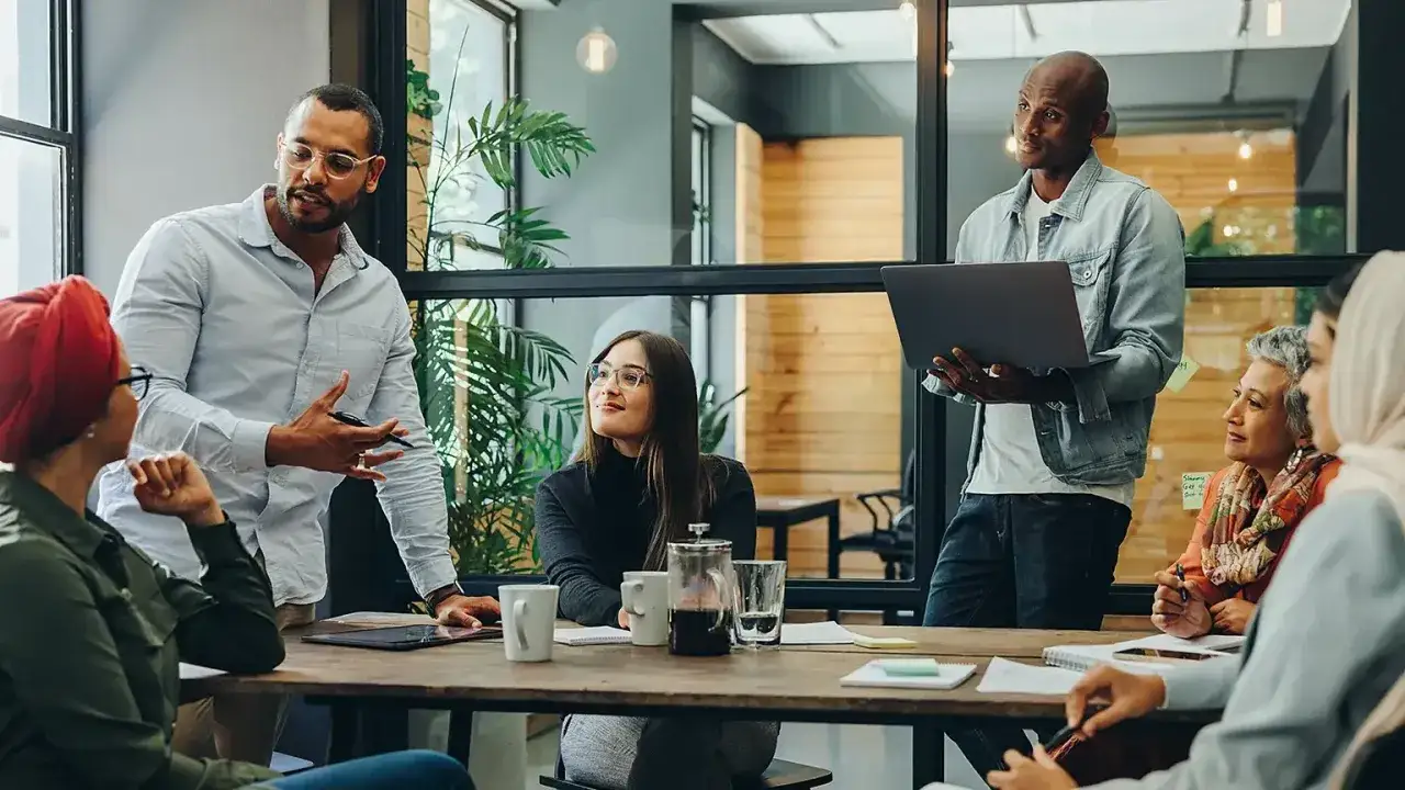 Ein diverses Team bespricht Ideen. Männer und Frauen unterschiedlicher Herkunft und Altersgruppen arbeiten zusammen. Tolle diversity beispiele!